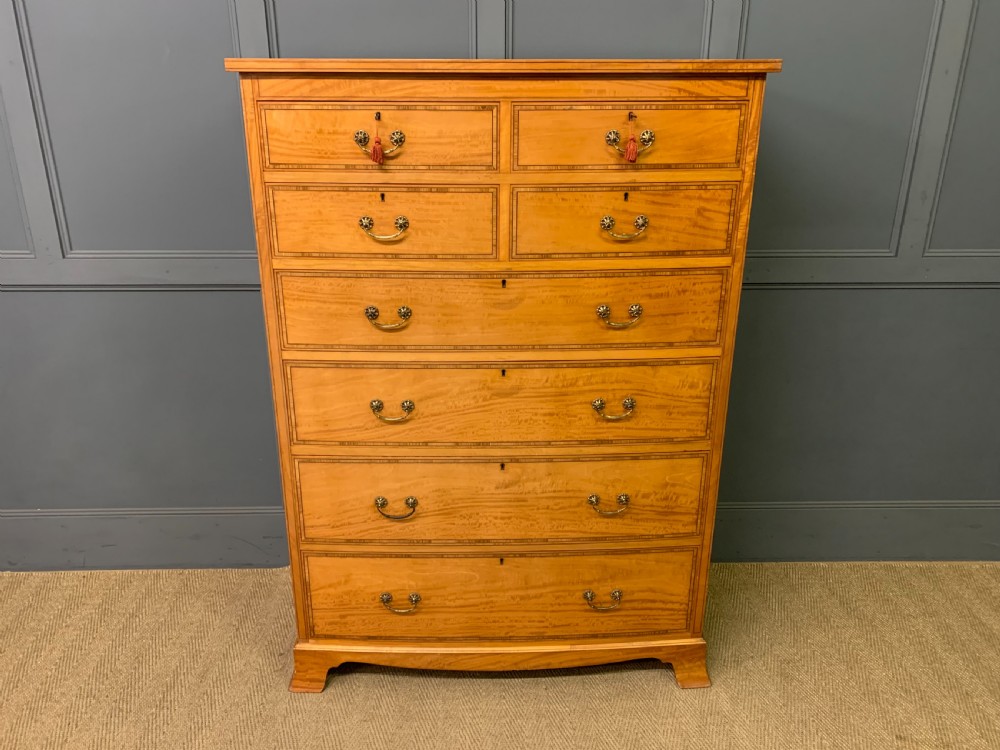 A tall satinwood chest of drawers featuring eight inlaid drawers with brass swan-neck handles and bracket feet. View III