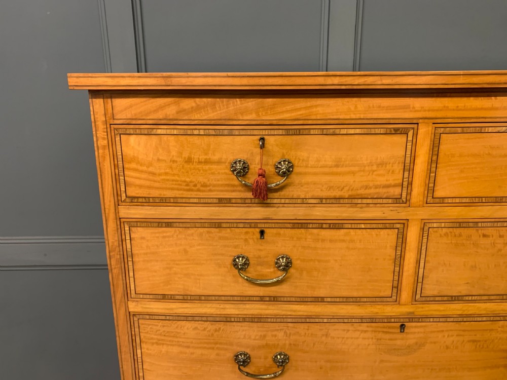 A tall satinwood chest of drawers featuring eight inlaid drawers with brass swan-neck handles and bracket feet. View IV