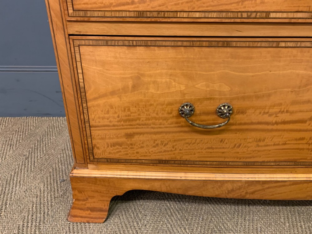 A tall satinwood chest of drawers featuring eight inlaid drawers with brass swan-neck handles and bracket feet. View VI