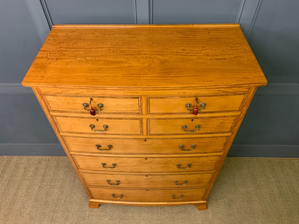 A tall satinwood chest of drawers featuring eight inlaid drawers with brass swan-neck handles and bracket feet. View IX