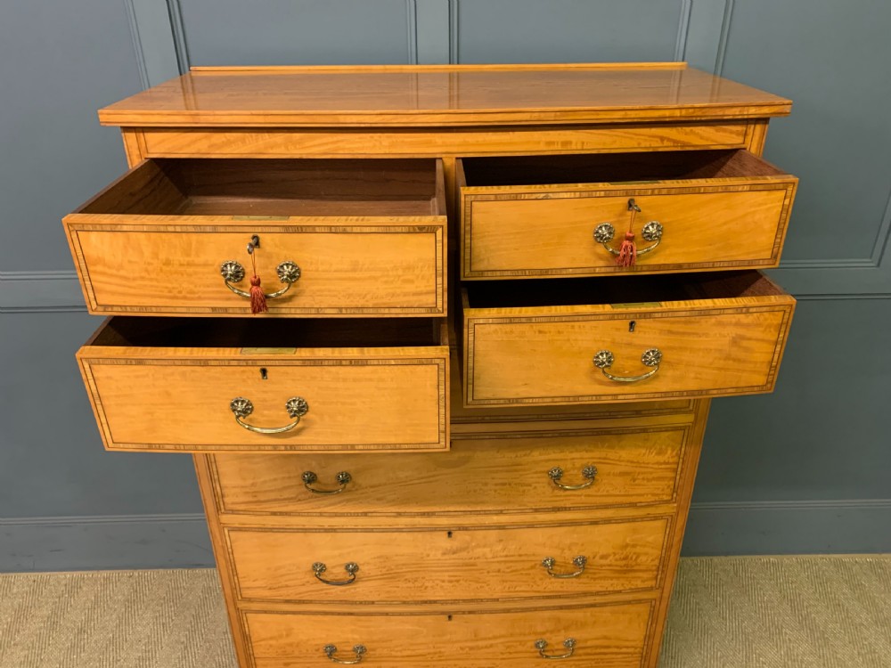 A tall satinwood chest of drawers featuring eight inlaid drawers with brass swan-neck handles and bracket feet. View X