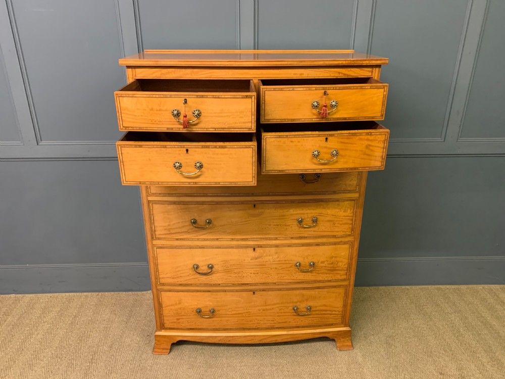 A tall satinwood chest of drawers featuring eight inlaid drawers with brass swan-neck handles and bracket feet. View XI