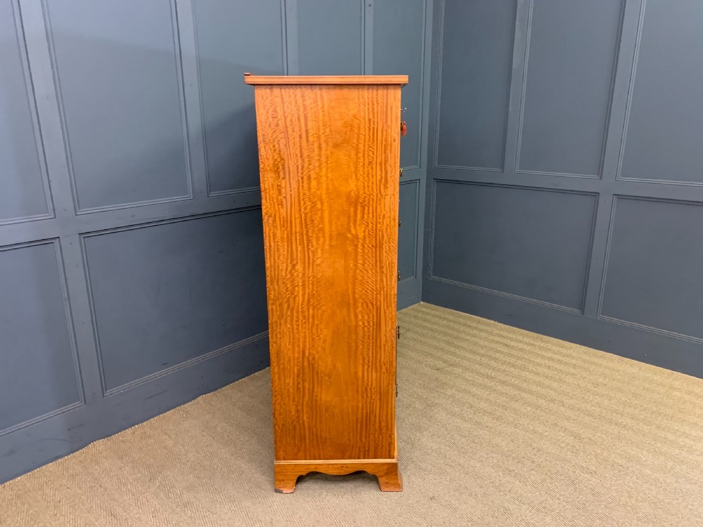 A tall satinwood chest of drawers featuring eight inlaid drawers with brass swan-neck handles and bracket feet. View XIV