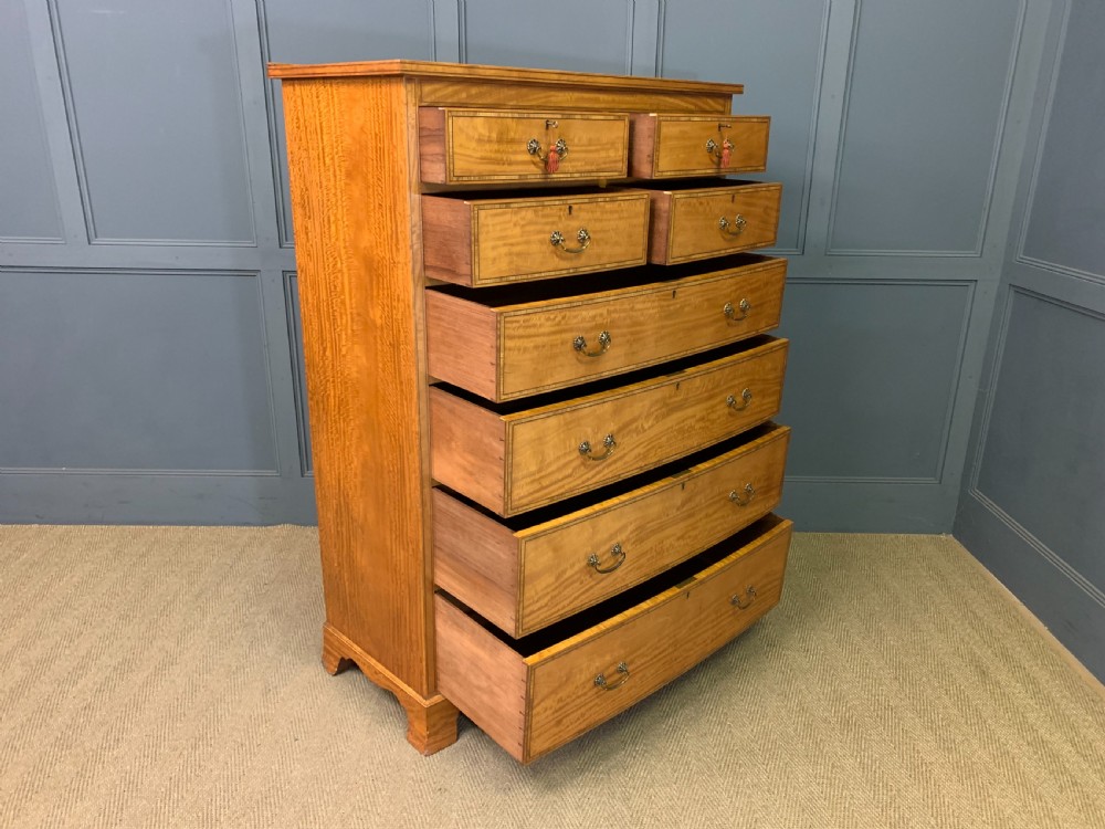 A tall satinwood chest of drawers featuring eight inlaid drawers with brass swan-neck handles and bracket feet. View XV