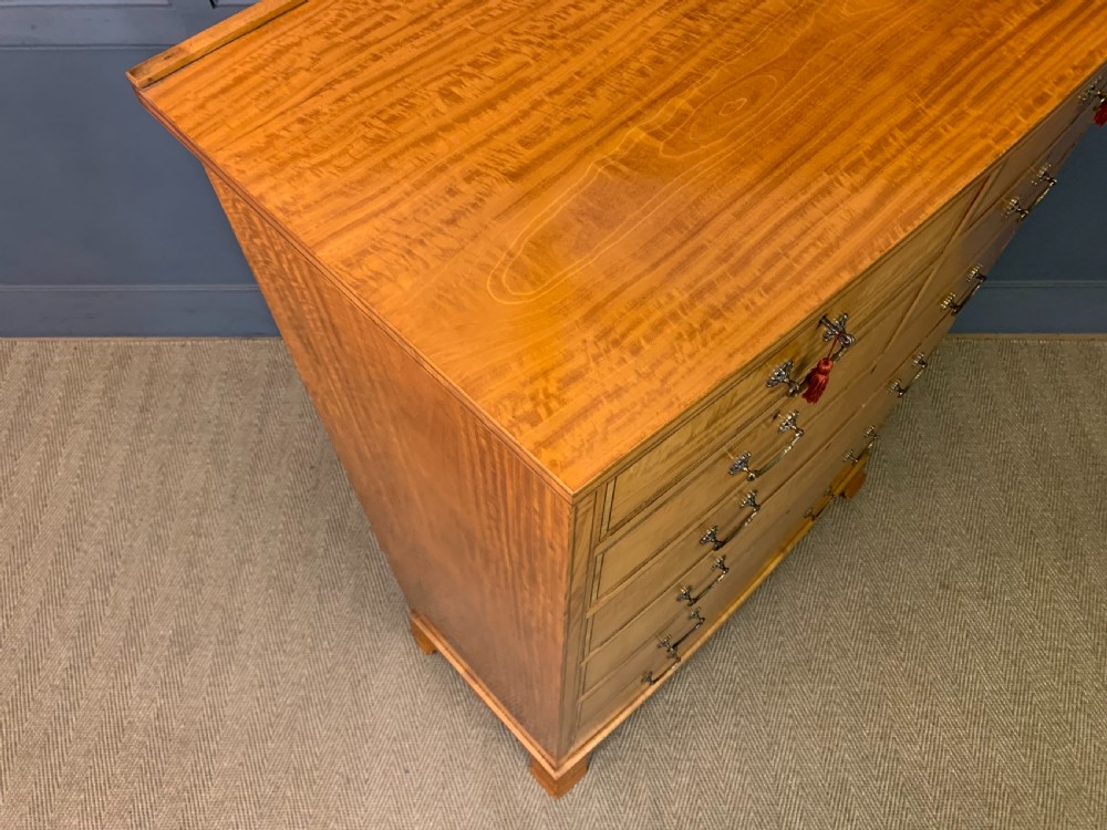 A tall satinwood chest of drawers featuring eight inlaid drawers with brass swan-neck handles and bracket feet. View XVII