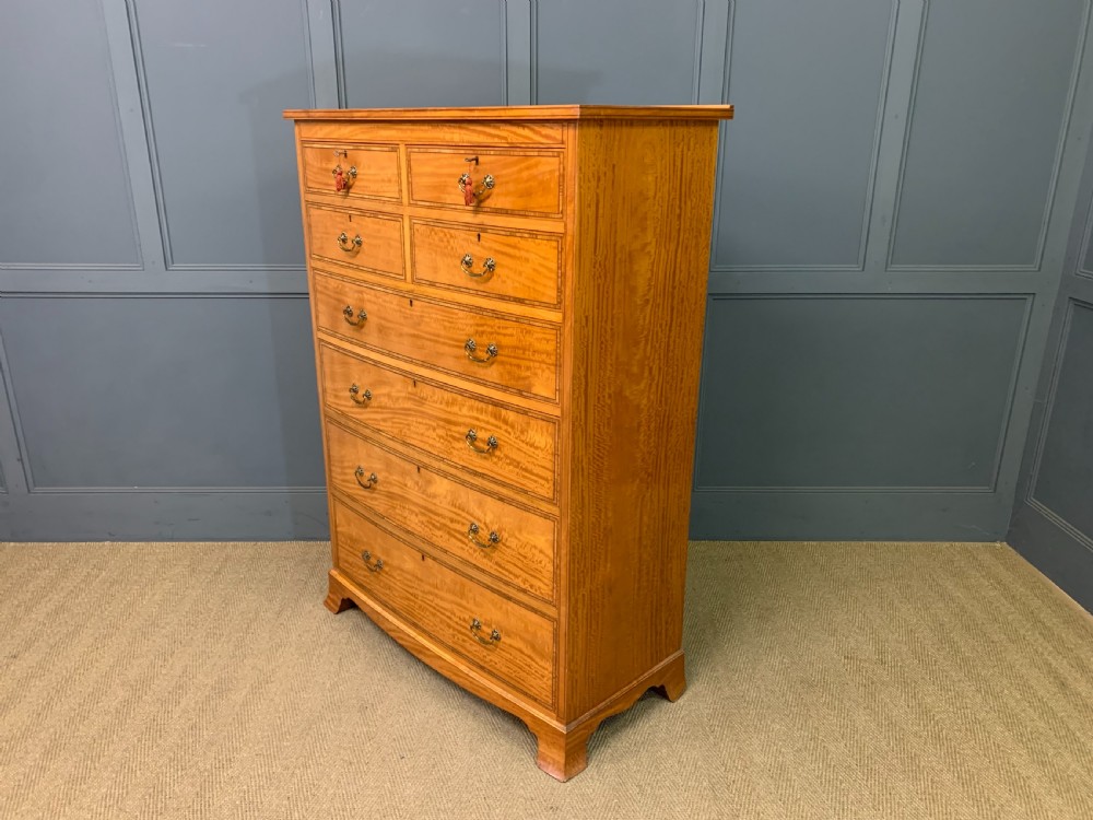 A tall satinwood chest of drawers featuring eight inlaid drawers with brass swan-neck handles and bracket feet. View XVIII