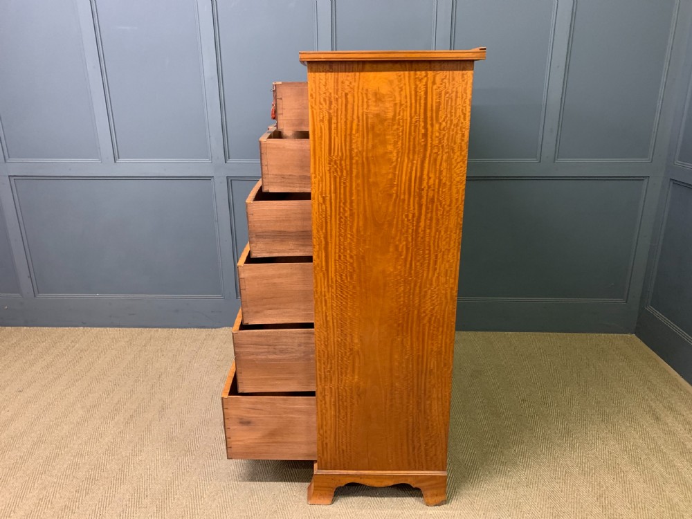 A tall satinwood chest of drawers featuring eight inlaid drawers with brass swan-neck handles and bracket feet. View XIX