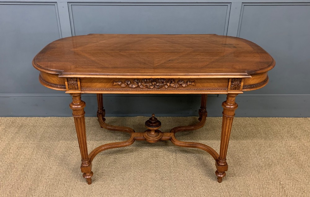 A 19th-century French walnut centre table featuring a parquet veneered top, carved floral frieze, fluted turned legs, and a shaped X-stretcher with a central finial.