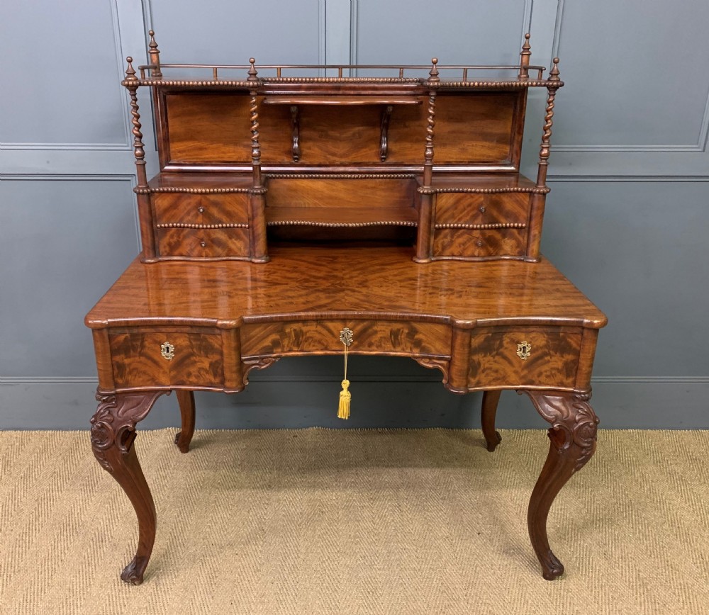 A flame mahogany writing desk featuring carved cabriole legs, a raised superstructure with drawers and gallery shelves, and a curved front with brass keyholes.