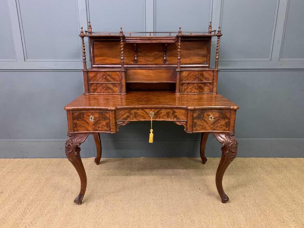 A flame mahogany writing desk featuring carved cabriole legs, a raised superstructure with drawers and gallery shelves, and a curved front with brass keyholes. View II
