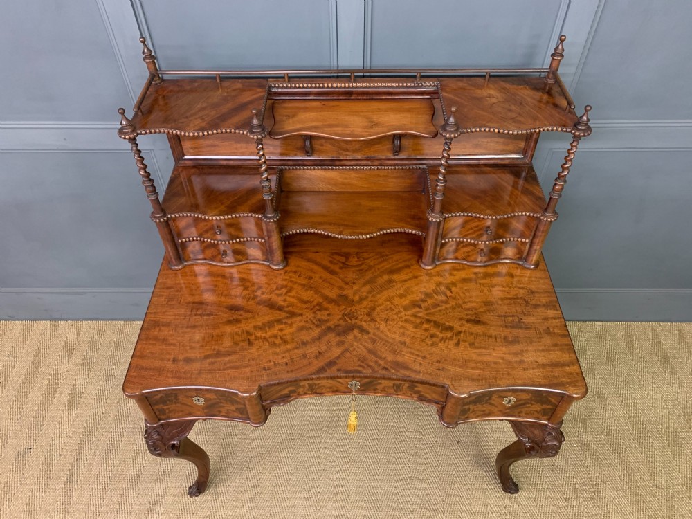 A flame mahogany writing desk featuring carved cabriole legs, a raised superstructure with drawers and gallery shelves, and a curved front with brass keyholes. View III