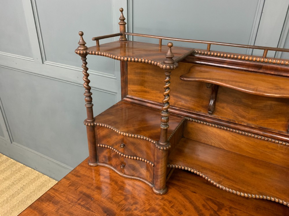 A flame mahogany writing desk featuring carved cabriole legs, a raised superstructure with drawers and gallery shelves, and a curved front with brass keyholes. View VII