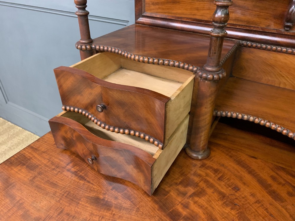 A flame mahogany writing desk featuring carved cabriole legs, a raised superstructure with drawers and gallery shelves, and a curved front with brass keyholes. View IX