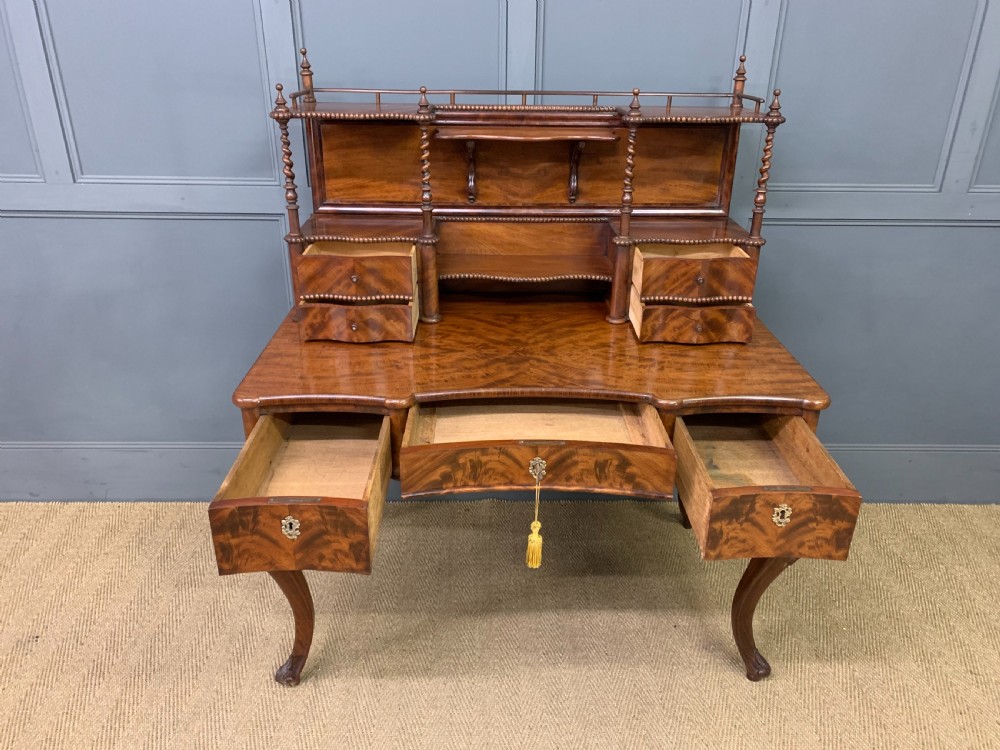 A flame mahogany writing desk featuring carved cabriole legs, a raised superstructure with drawers and gallery shelves, and a curved front with brass keyholes. View X