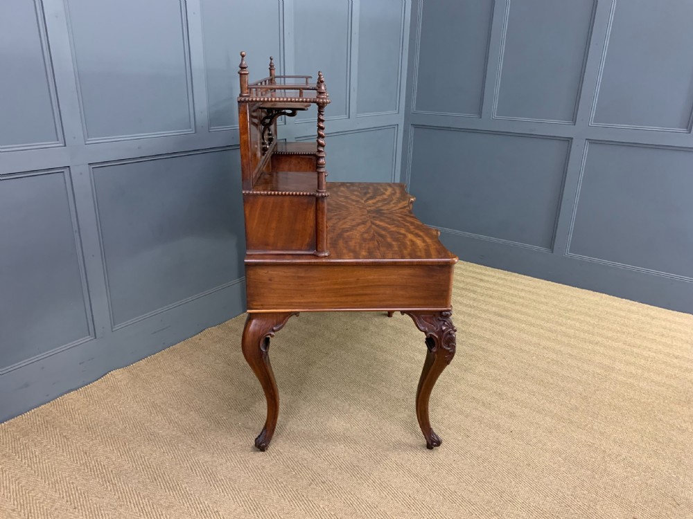 A flame mahogany writing desk featuring carved cabriole legs, a raised superstructure with drawers and gallery shelves, and a curved front with brass keyholes. View XII