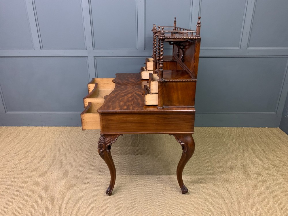 A flame mahogany writing desk featuring carved cabriole legs, a raised superstructure with drawers and gallery shelves, and a curved front with brass keyholes. View XVII