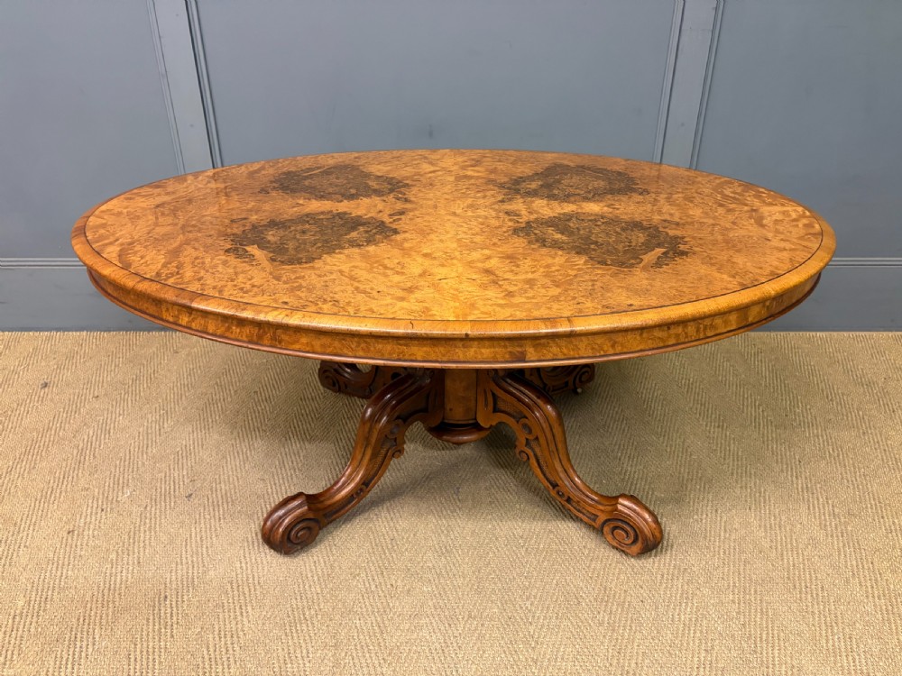 An oval Victorian coffee table crafted from figured burr walnut, featuring a carved four-legged pedestal base and scroll feet. View II