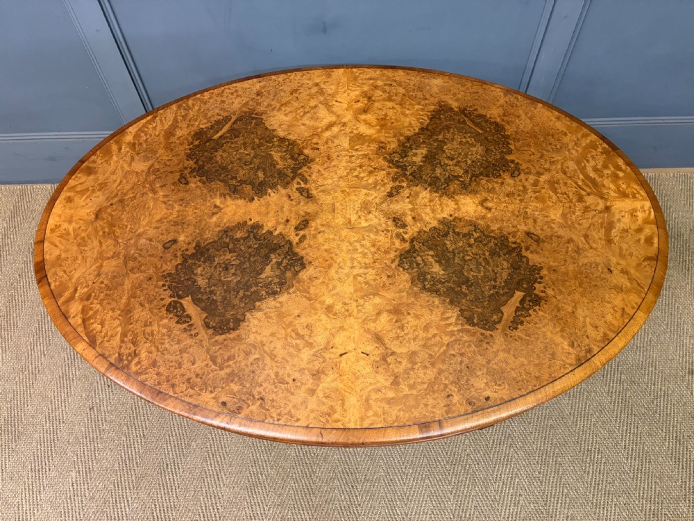 An oval Victorian coffee table crafted from figured burr walnut, featuring a carved four-legged pedestal base and scroll feet. View V
