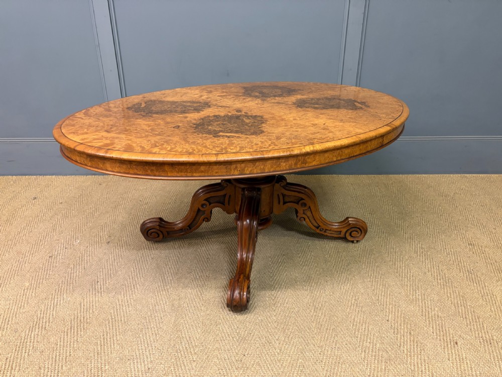 An oval Victorian coffee table crafted from figured burr walnut, featuring a carved four-legged pedestal base and scroll feet. View VII