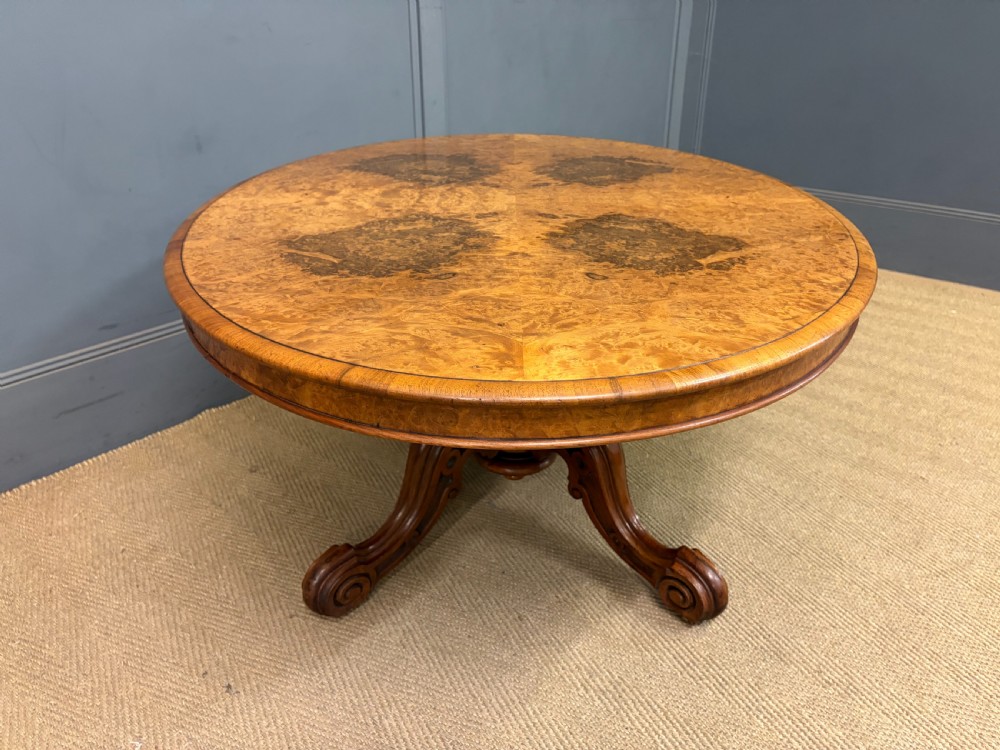 An oval Victorian coffee table crafted from figured burr walnut, featuring a carved four-legged pedestal base and scroll feet. View VIII