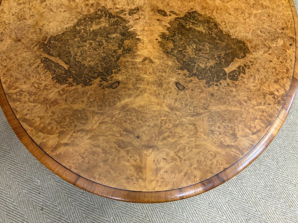 An oval Victorian coffee table crafted from figured burr walnut, featuring a carved four-legged pedestal base and scroll feet. View IX
