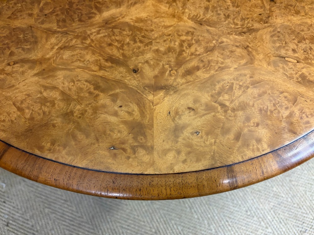 An oval Victorian coffee table crafted from figured burr walnut, featuring a carved four-legged pedestal base and scroll feet. View X