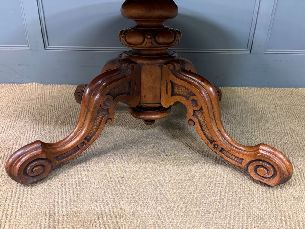An oval Victorian coffee table crafted from figured burr walnut, featuring a carved four-legged pedestal base and scroll feet. View XII
