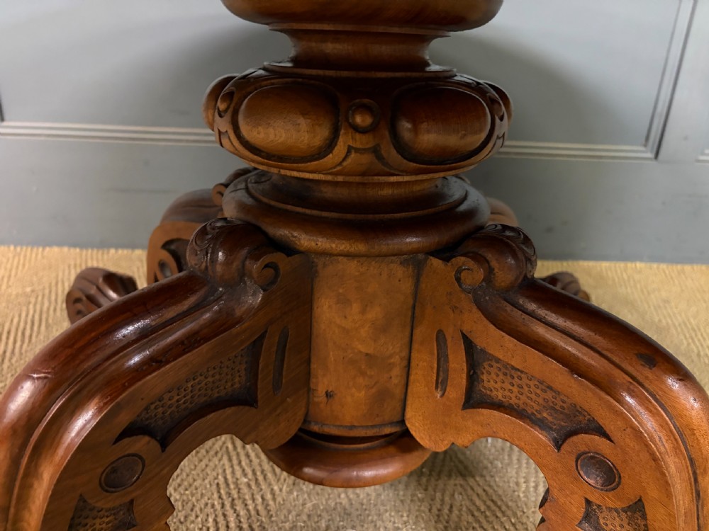An oval Victorian coffee table crafted from figured burr walnut, featuring a carved four-legged pedestal base and scroll feet. View XIV
