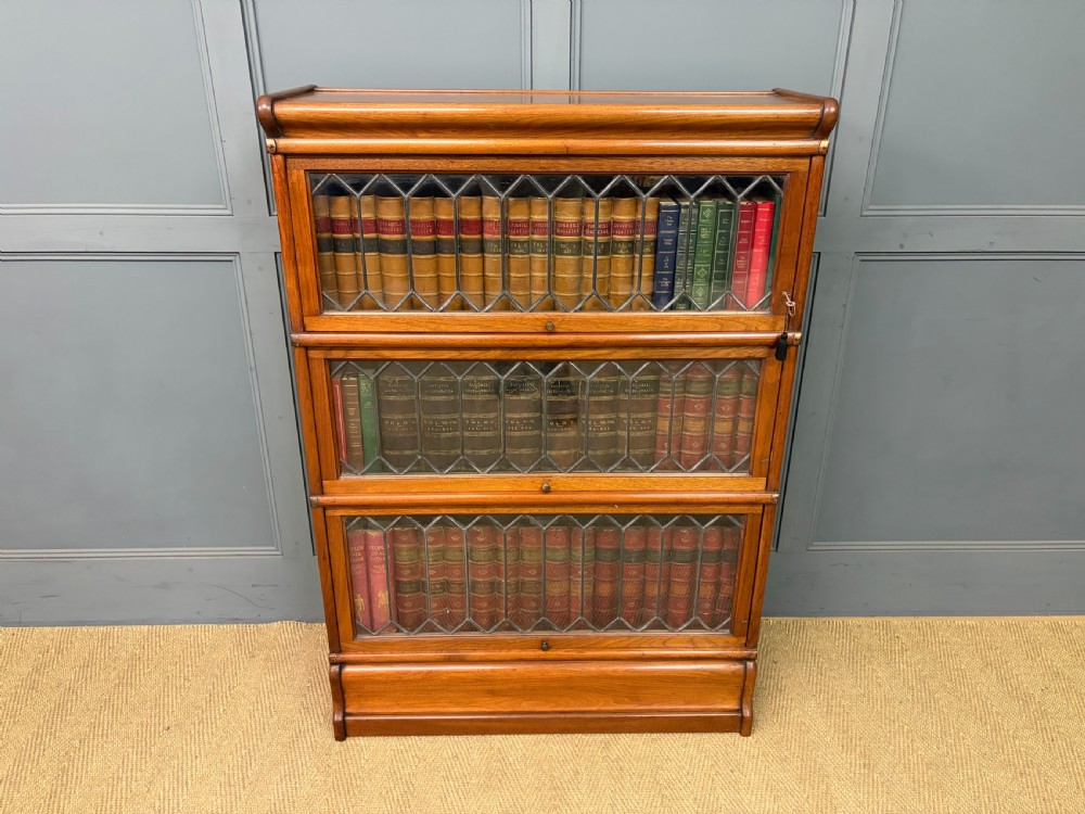 A three-tier walnut Globe Wernicke stacking bookcase featuring leaded glazed doors and a plinth base.