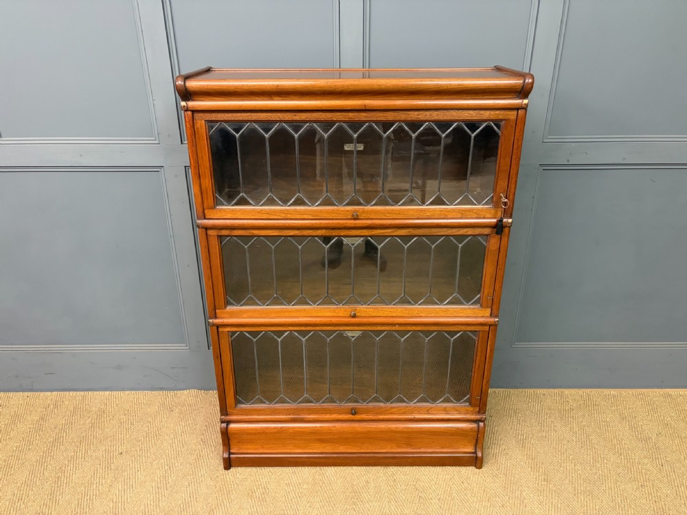 A three-tier walnut Globe Wernicke stacking bookcase featuring leaded glazed doors and a plinth base. View IV