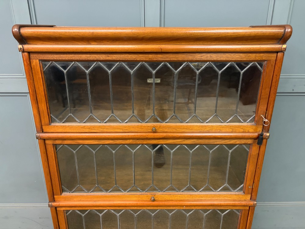 A three-tier walnut Globe Wernicke stacking bookcase featuring leaded glazed doors and a plinth base. View V