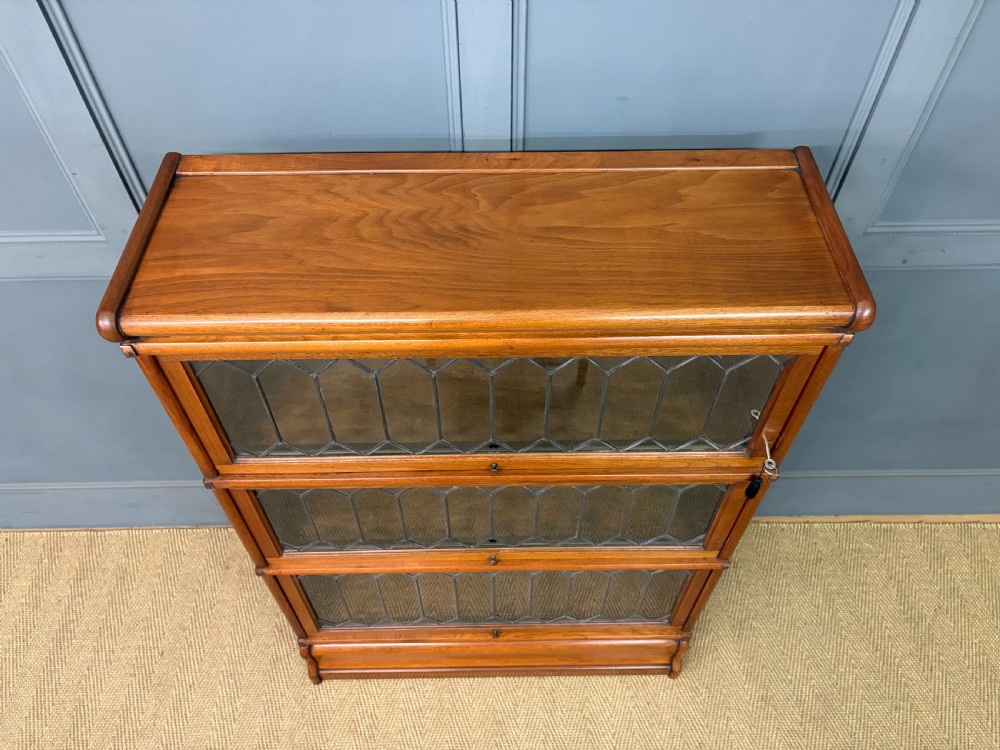 A three-tier walnut Globe Wernicke stacking bookcase featuring leaded glazed doors and a plinth base. View VI