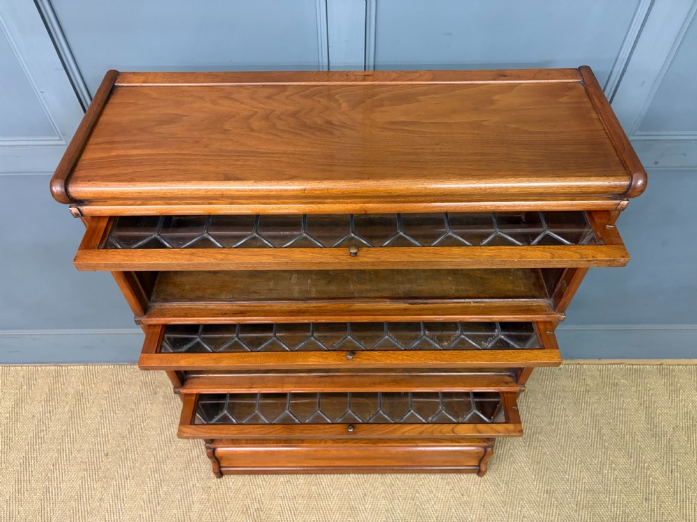 A three-tier walnut Globe Wernicke stacking bookcase featuring leaded glazed doors and a plinth base. View X