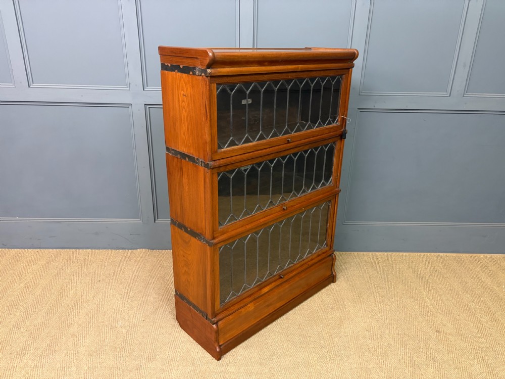 A three-tier walnut Globe Wernicke stacking bookcase featuring leaded glazed doors and a plinth base. View XII