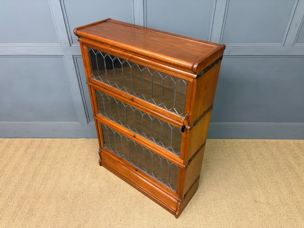 A three-tier walnut Globe Wernicke stacking bookcase featuring leaded glazed doors and a plinth base. View XIV