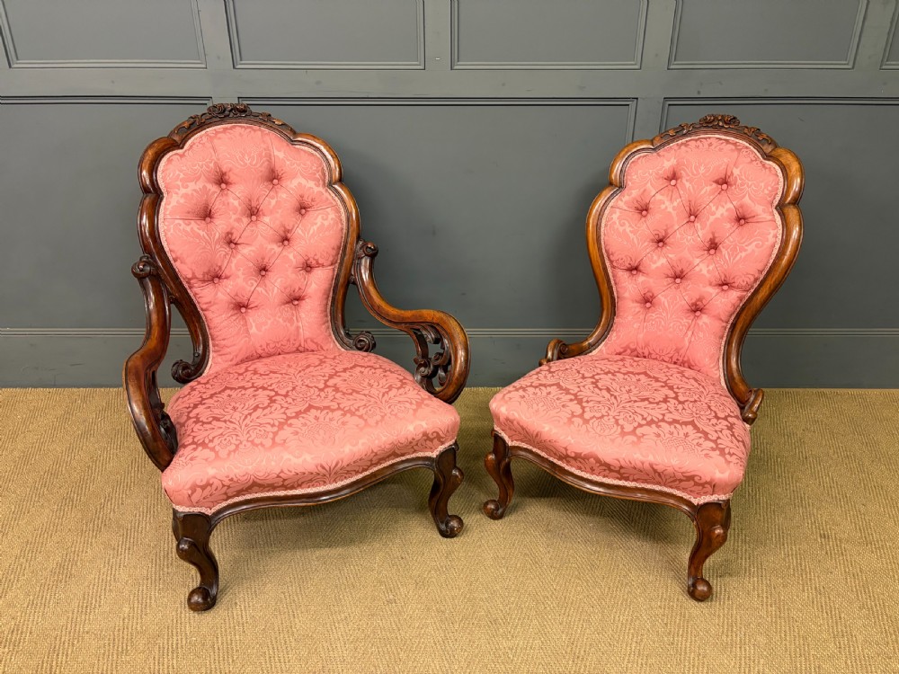 A pair of mid-Victorian carved walnut nursing chairs upholstered in buttoned pink damask fabric with cabriole legs.