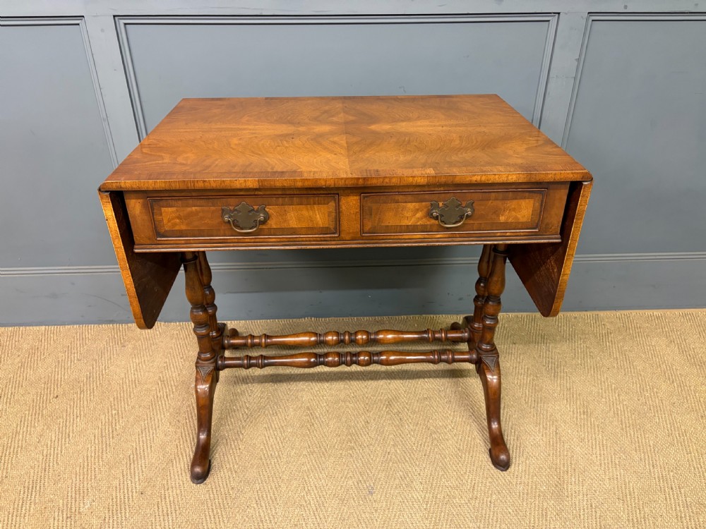 A burr walnut sofa table featuring twin drop leaves, two front drawers with brass handles, and double turned stretchers.