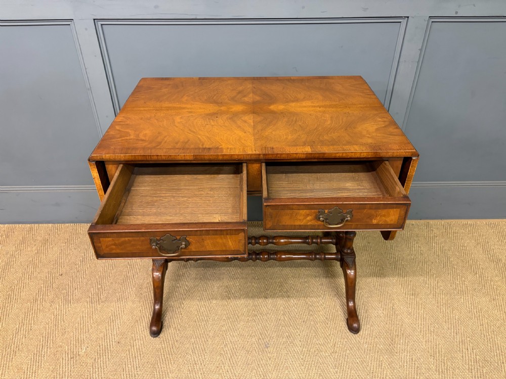 A burr walnut sofa table featuring twin drop leaves, two front drawers with brass handles, and double turned stretchers. View IV