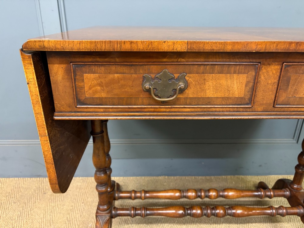A burr walnut sofa table featuring twin drop leaves, two front drawers with brass handles, and double turned stretchers. View V