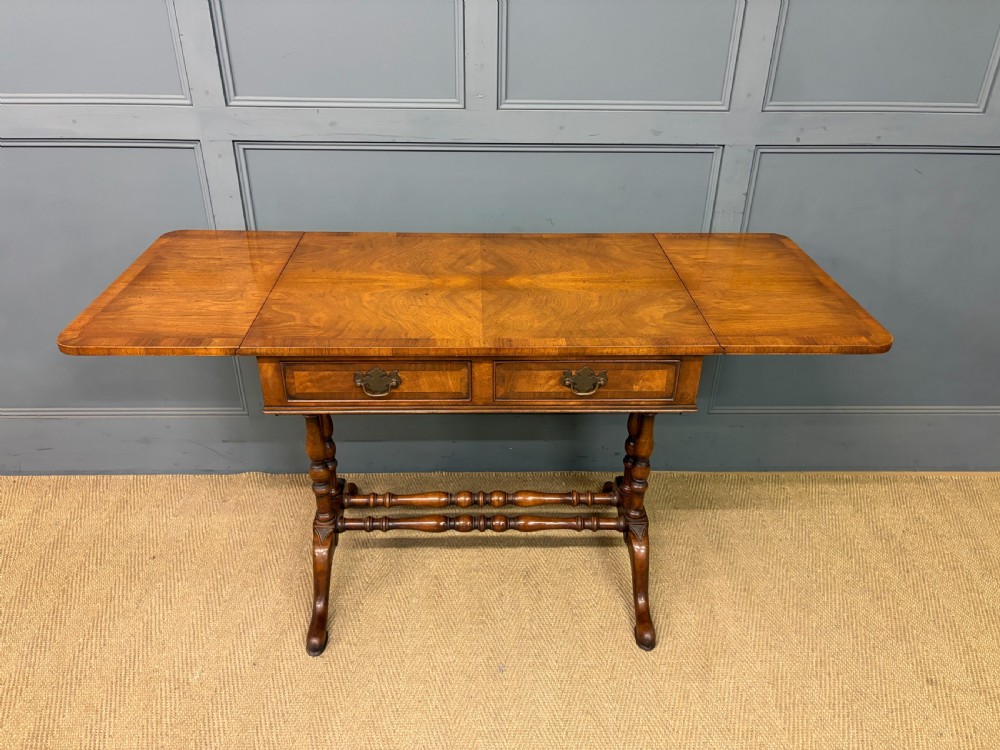 A burr walnut sofa table featuring twin drop leaves, two front drawers with brass handles, and double turned stretchers. View VI