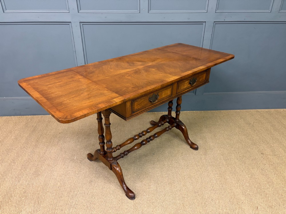 A burr walnut sofa table featuring twin drop leaves, two front drawers with brass handles, and double turned stretchers. View VIII
