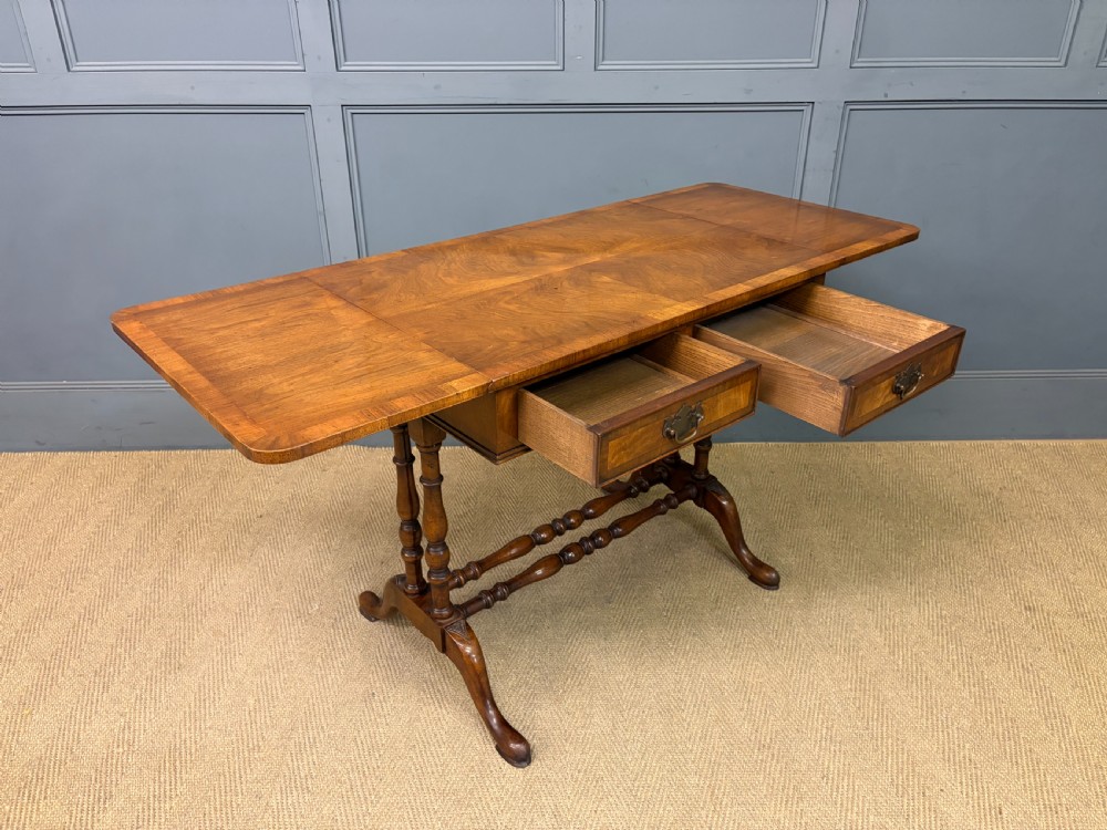 A burr walnut sofa table featuring twin drop leaves, two front drawers with brass handles, and double turned stretchers. View X