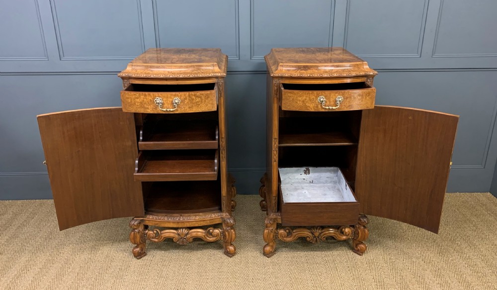 A pair of tall burr walnut pedestal cupboards featuring curved front doors, single top drawers with brass drop handles, and carved scroll feet. View V