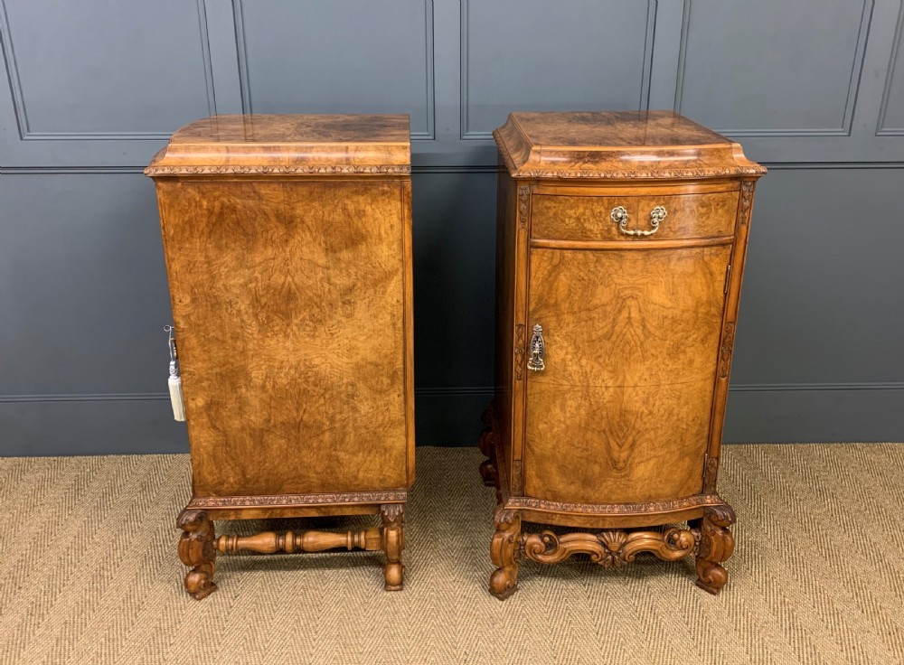 A pair of tall burr walnut pedestal cupboards featuring curved front doors, single top drawers with brass drop handles, and carved scroll feet. View VI