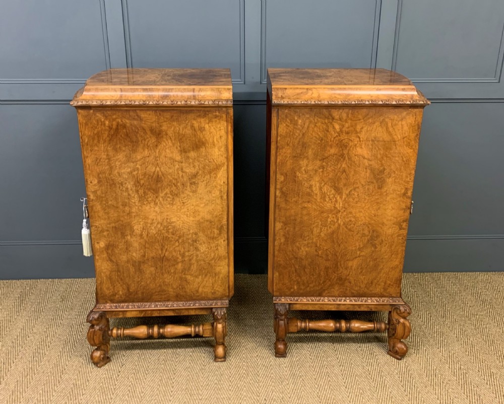 A pair of tall burr walnut pedestal cupboards featuring curved front doors, single top drawers with brass drop handles, and carved scroll feet. View VII