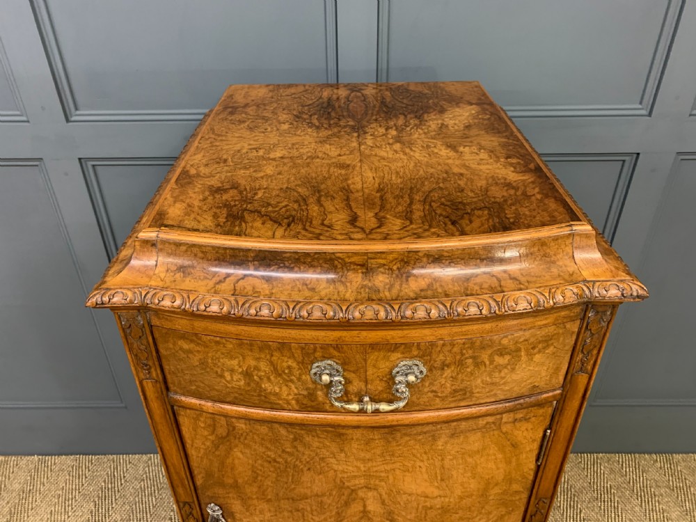 A pair of tall burr walnut pedestal cupboards featuring curved front doors, single top drawers with brass drop handles, and carved scroll feet. View X