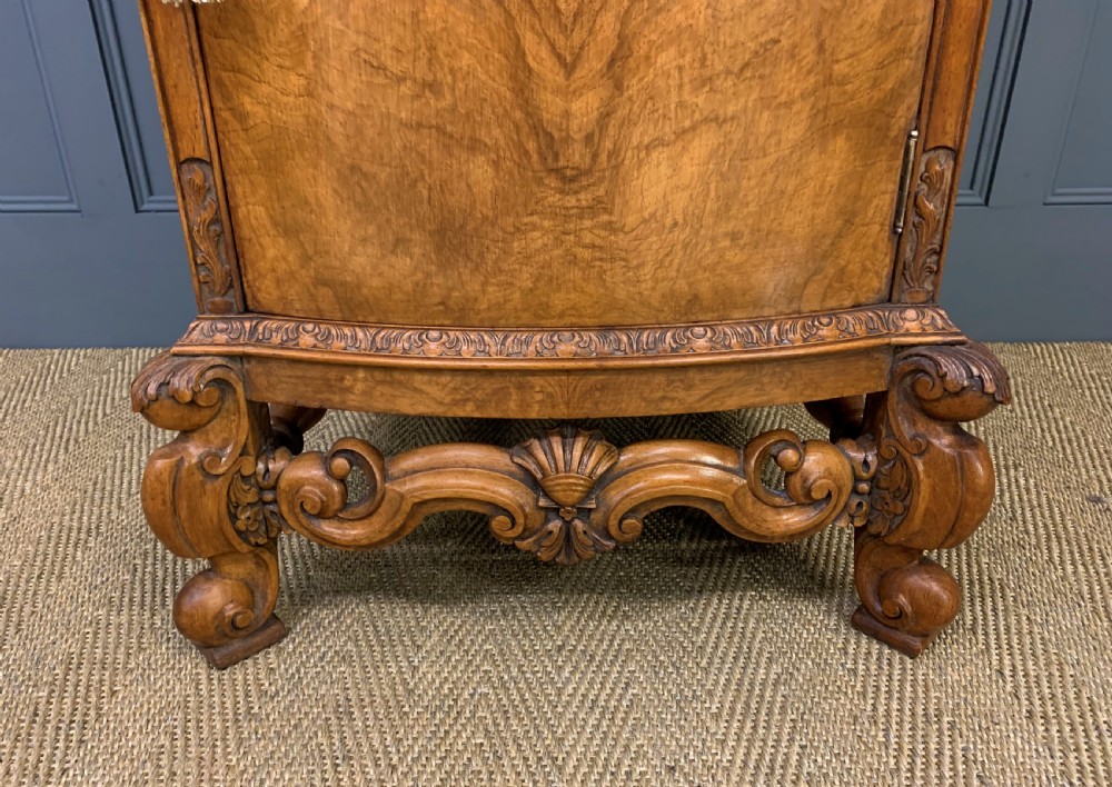A pair of tall burr walnut pedestal cupboards featuring curved front doors, single top drawers with brass drop handles, and carved scroll feet. View XI