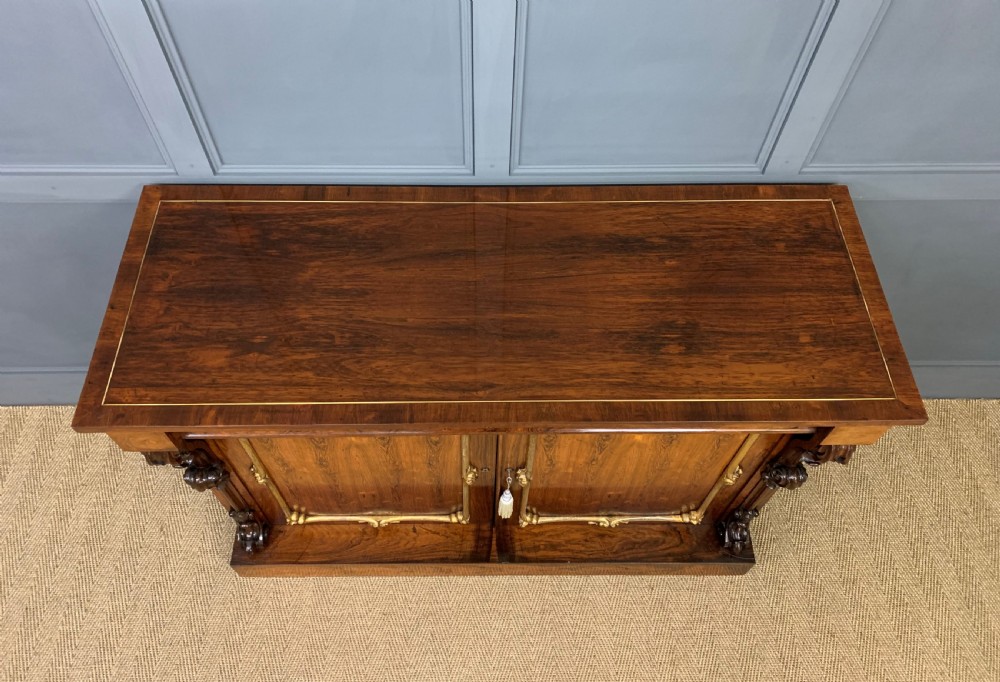 A dark Regency period rosewood side cabinet featuring two cupboard doors with gilded bronze trim and carved scroll supports on a plinth base. View IV