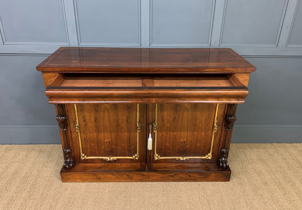 A dark Regency period rosewood side cabinet featuring two cupboard doors with gilded bronze trim and carved scroll supports on a plinth base. View V