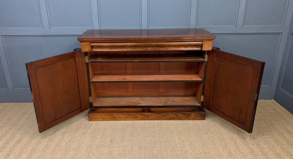 A dark Regency period rosewood side cabinet featuring two cupboard doors with gilded bronze trim and carved scroll supports on a plinth base. View VII